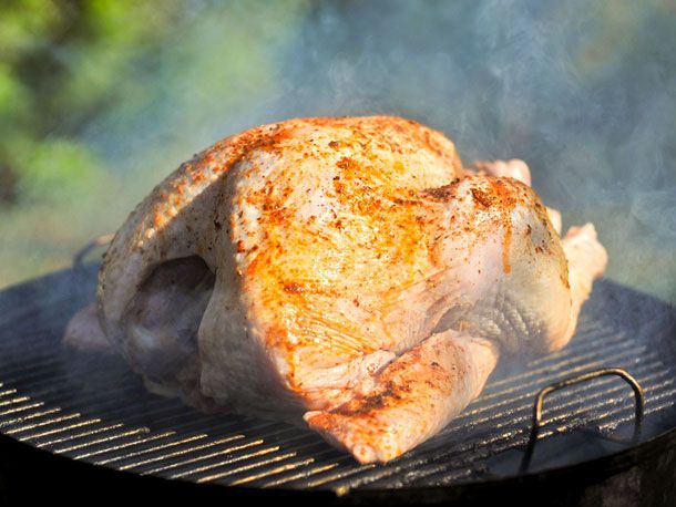 A spice-rubbed turkey placed on the surface of a smoking charcoal grill.