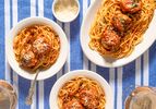 Plates of spaghetti with chicken parmesan meatballs on a blue striped tablecloth
