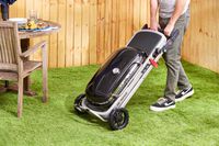 A person in a backyard wheeling the Weber Traveler Portable Gas Grill