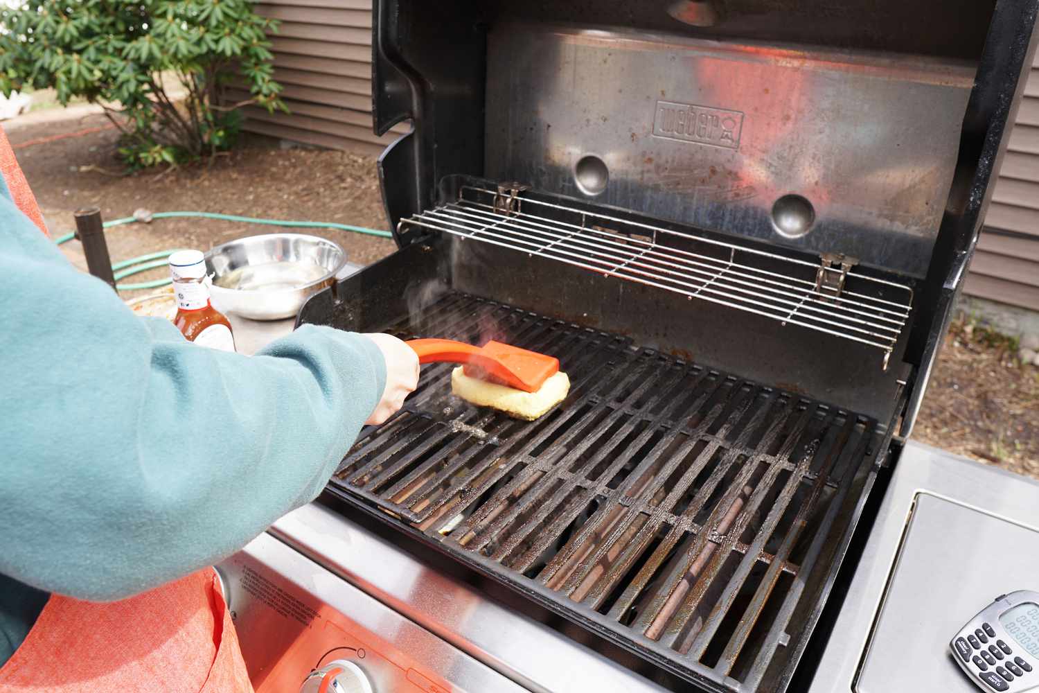 A person using a grill brush to clean a hot grill