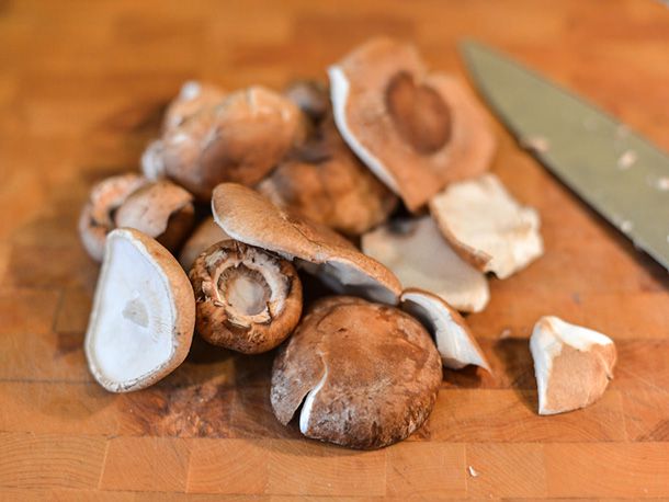 Fresh creminis and shiitakes on a wooden cutting board with a knife.