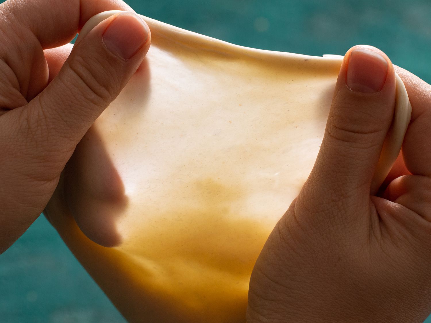 Two hands pulling apart a piece of scallion pancake dough to demonstrate the "window pane test."