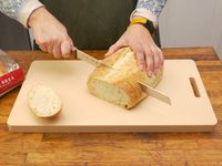 A person slicing crusty bread on the yoshihiro cutting board