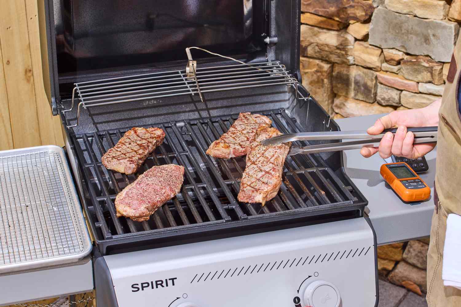 A hand using tongs to lift steak on the Weber Spirit E-210 Gas Grill