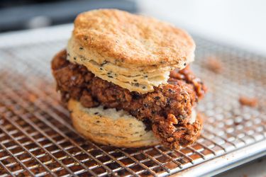 A kimchi fried chicken black sesame biscuit sandwich on a wire rack set over a rimmed baking sheet