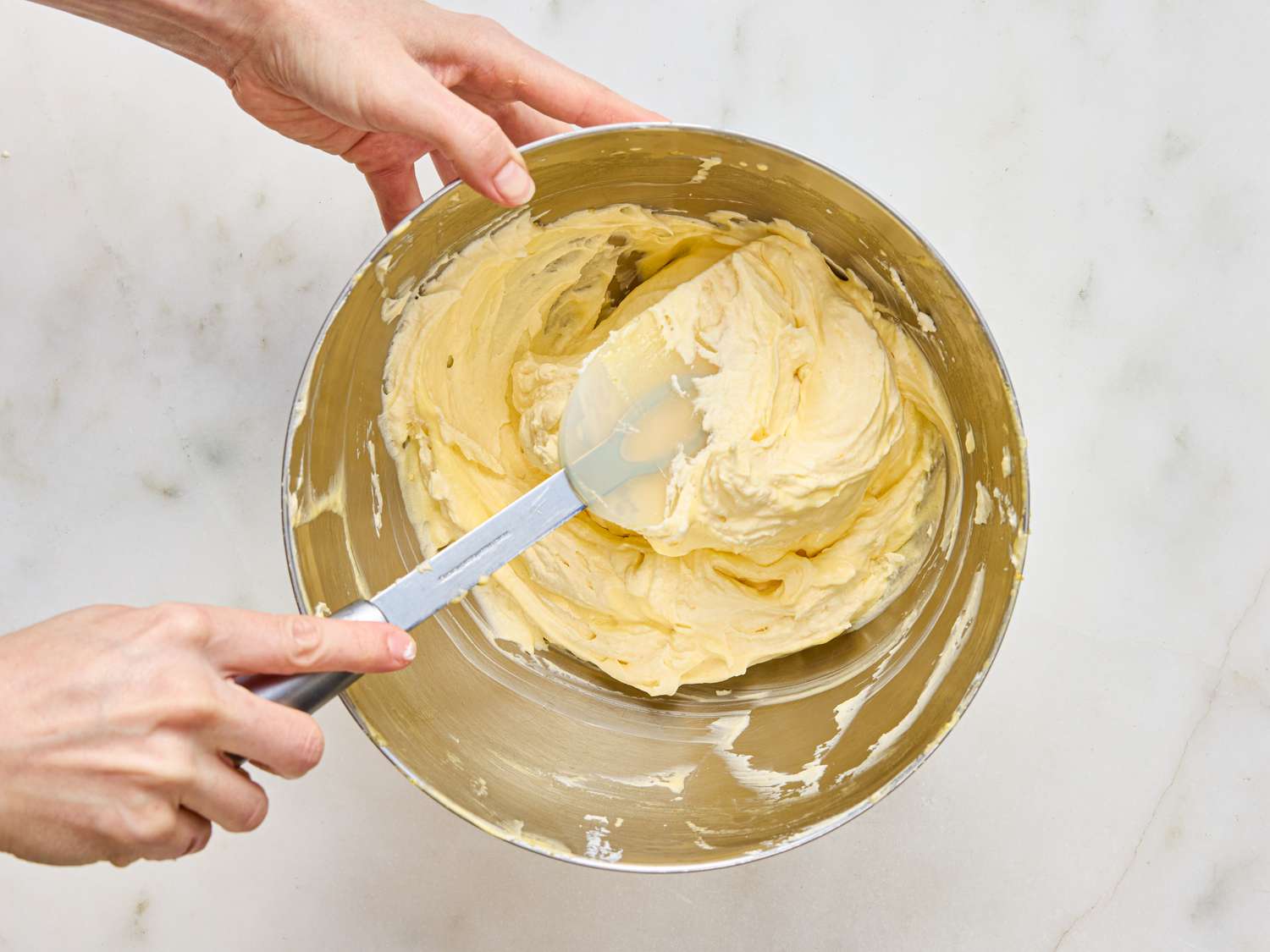 Hands mixing dessert batter in a metal bowl with a spatula