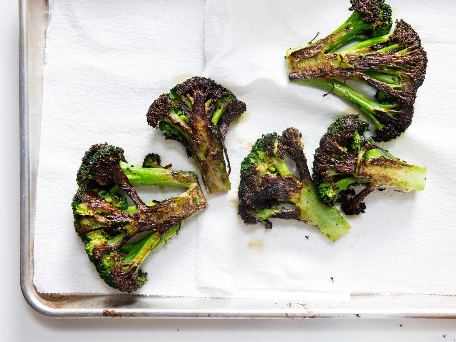 Charred broccoli pieces on a paper towel–lined baking sheet.