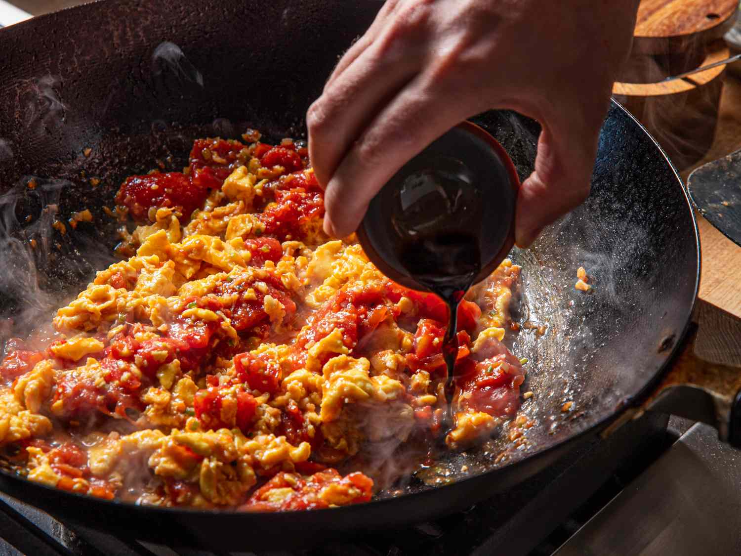Ingredients being cooked in a pan with a liquid being poured in by hand