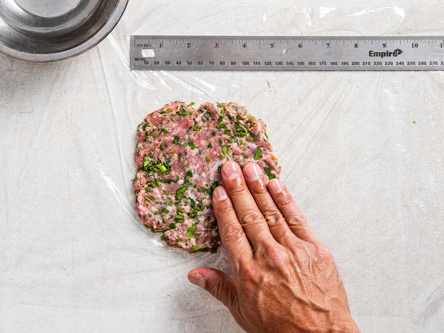 Pressing meat mixture into a flat patty on plastic wrap 