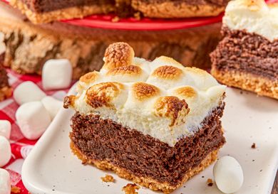 A slice of brownie topped with toasted marshmallows on a plate surrounded by mini marshmallows