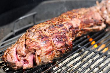 Closeup of a whole beef tenderloin cooking on a charcoal grill.