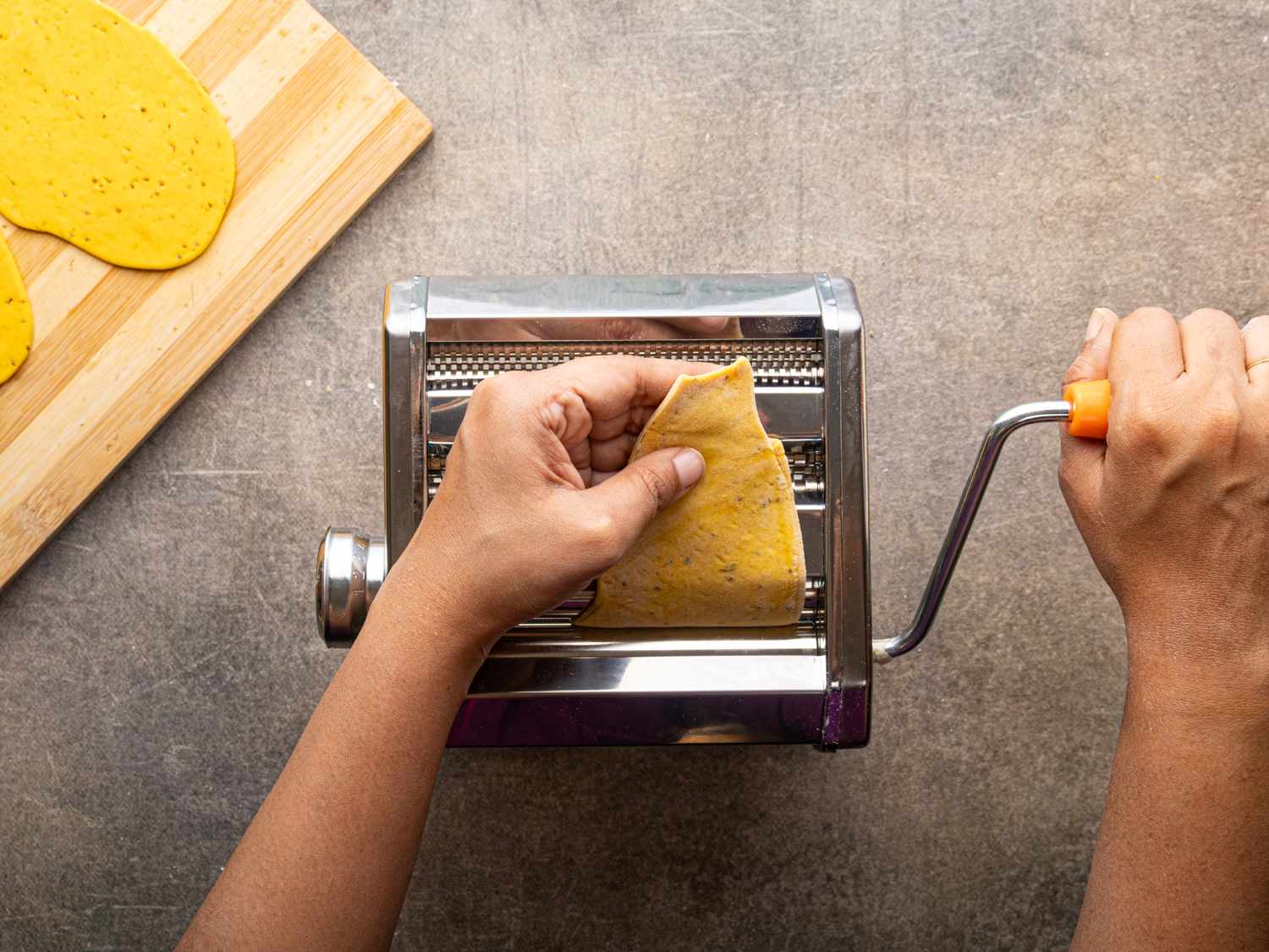 Person using a pasta machine to roll out dough