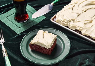 piece of guinnes chocolate cake taken from corner of sheetpan and placed on a green plate. Side of beer on green napkin, green fork, on top of green fabric