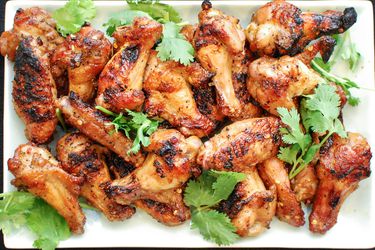 Overhead view of Grilled Spicy Chicken Wings With Soy and Fish Sauce piled on a square white platter, garnished with cilantro leaves.