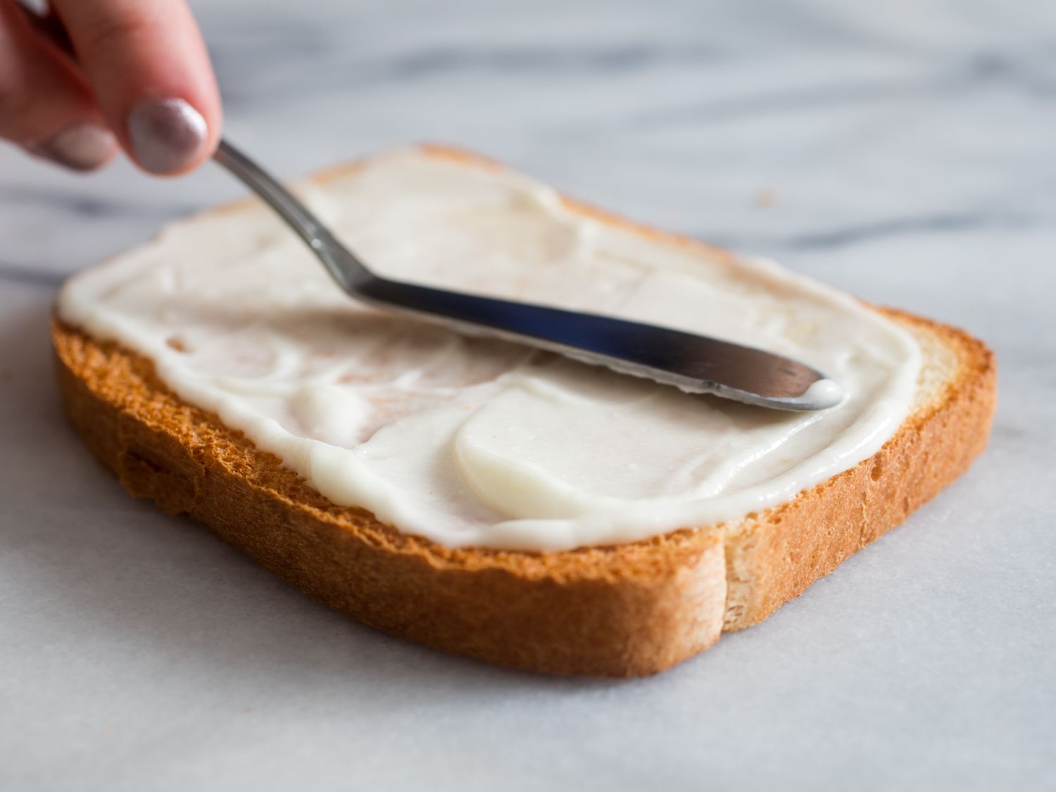 Egg white mayonnaise is spread on a slice of white sandwich bread.