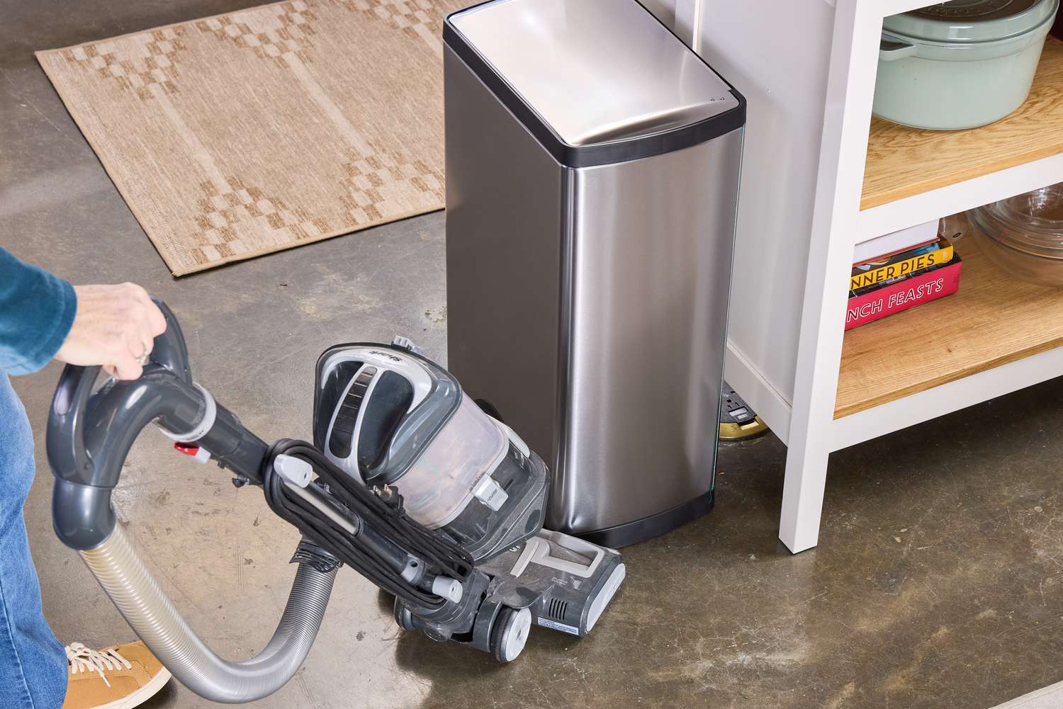 A person vacuums the area around the simplehuman 38-Liter Brushed Stainless Steel Steel Trash Can with Lid