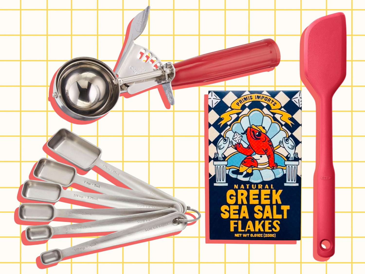 A set of kitchen tools including stainless steel measuring spoons an ice cream scoop a spatula and a box of Greek sea salt flakes