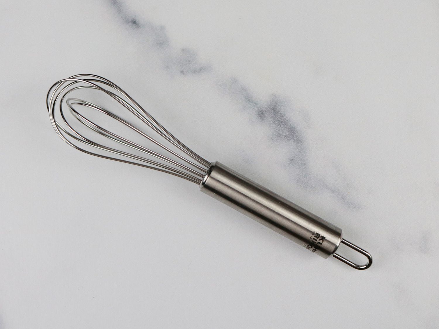 a miniature whisk on a white marble background