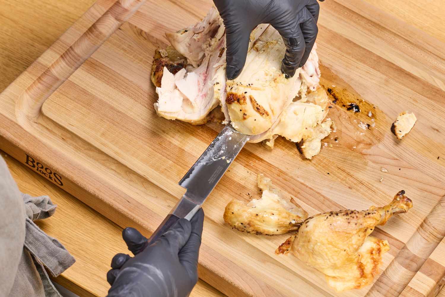 Gloved hands carving a roasted chicken on a John Boos Reversible Maple Wood Cutting Board with Juice Groove