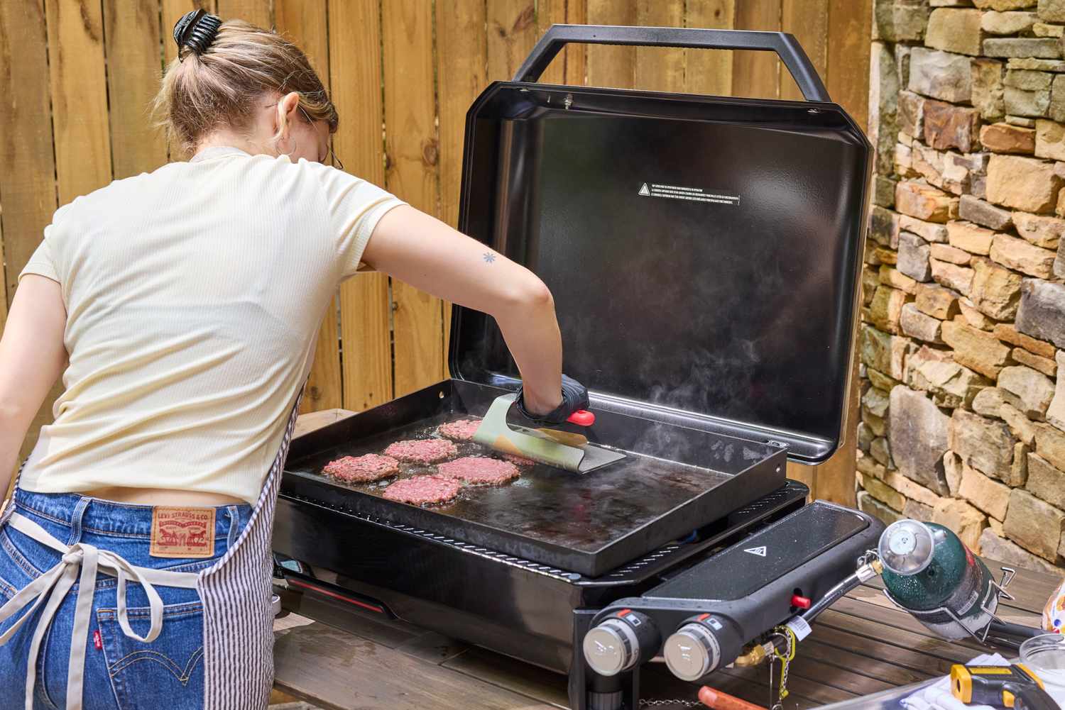 A person makes hamburgers using the Weber Slate 22 inch Rust-Resistant Tabletop Griddle