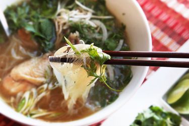 A bowl of pho ga. A pair of chopsticks are holding some noodles above the bowl. 