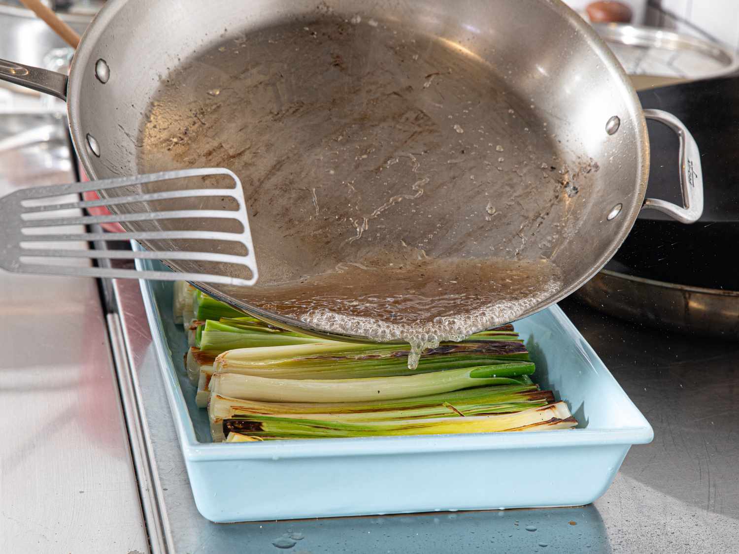 Side view of pouring skillet water over leeks