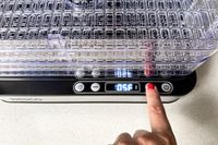 A person pressing the power button on a Nesco Digital 5 Rectangular Dehydrator set to 105 degrees Fahrenheit