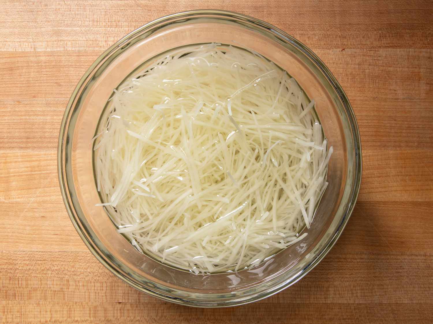 Shredded potato strands in a bowl of water.