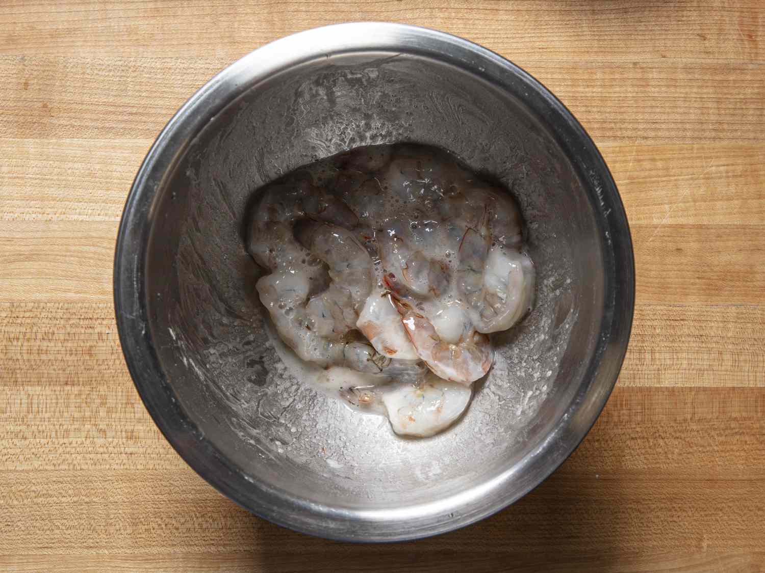 Shrimp coated with potato starch mixture in a metal bowl.