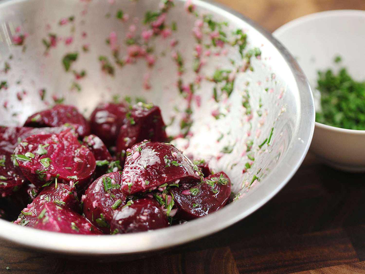 A metal bowl of roasted beet cut into chunks and tossed in dressing and fresh herbs.