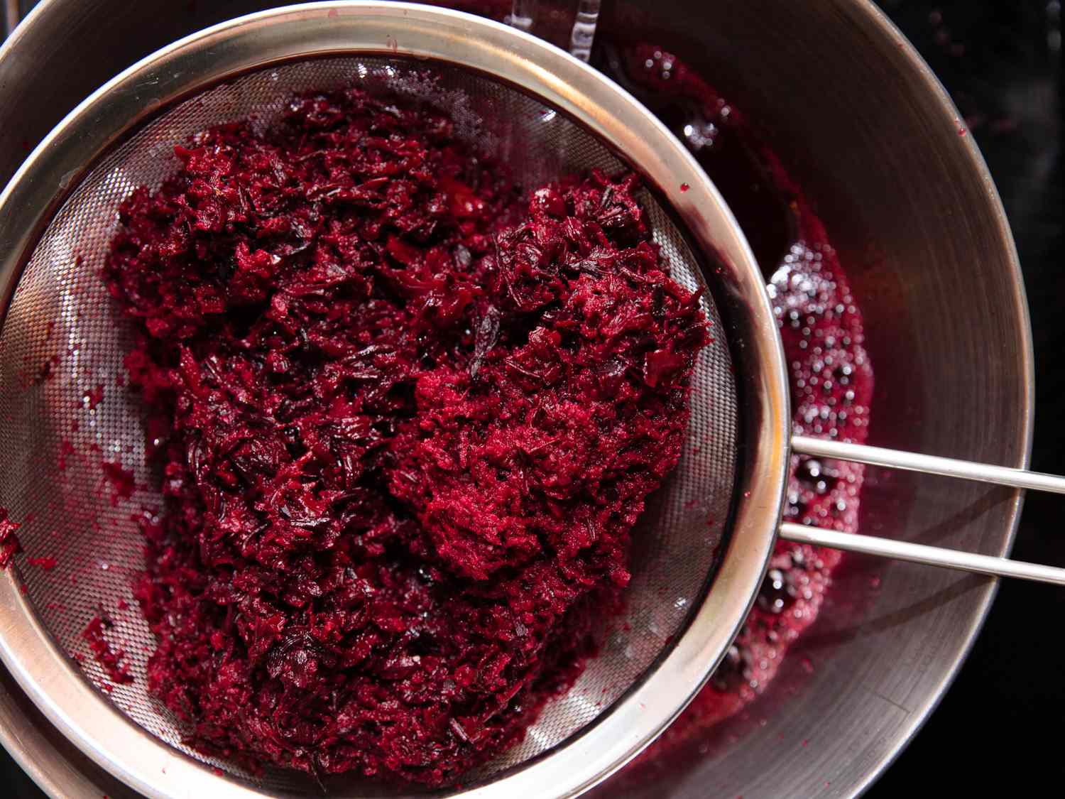 Water, sorrel, grated ginger, cloves, and crushed allspice mixture being strained through a metal strainer.