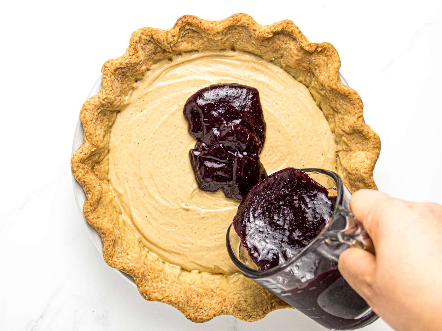 Hand pouring jelly onto a peanut butter pie in progress