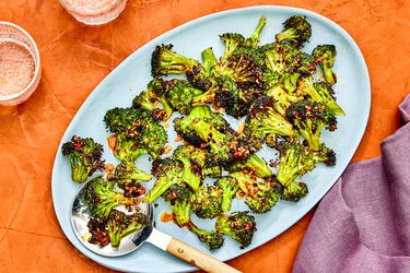Air-fried broccoli with chili crisp on a blue platter against an orange background.
