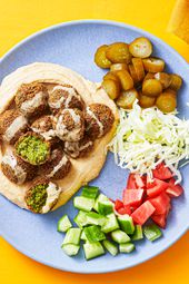 Plated pita bread stuffed with falafels, tahini, tomatoes, cucumber, pickles, and shredded cabbage