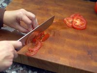 someone cutting a tomato on a wooden cutting board 