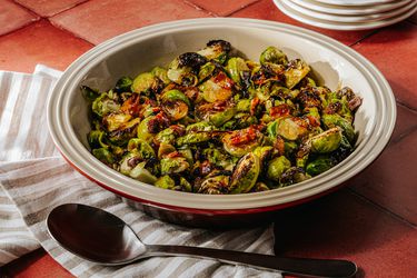 Bowl of roasted brussel sprouts on a brick surface, with a striped towl and spoon 