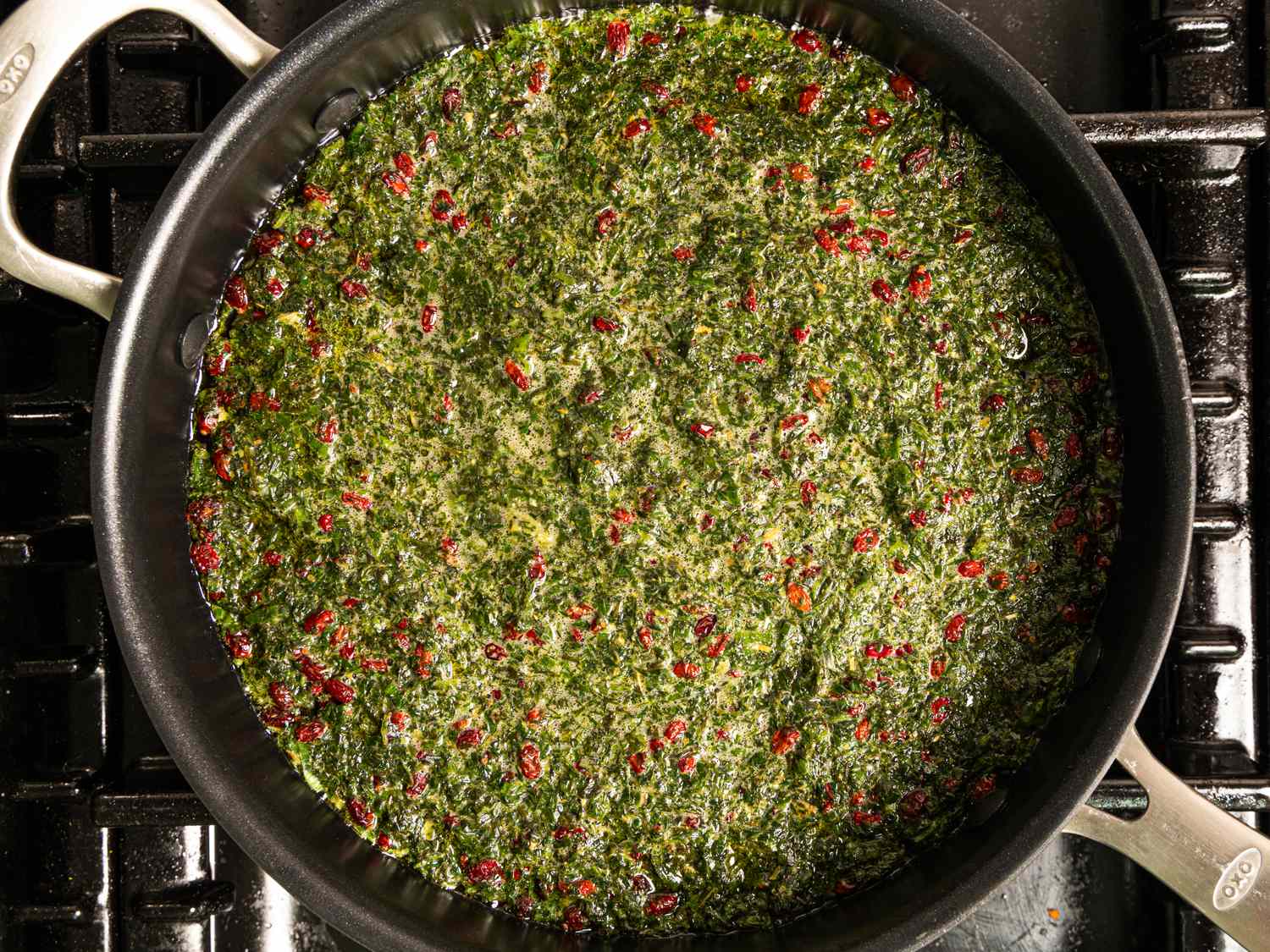 A pan with a green herb and red berry dish cooking on a stove