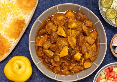 A dish of khoreshe beh alongside sides like rice and other accompaniments