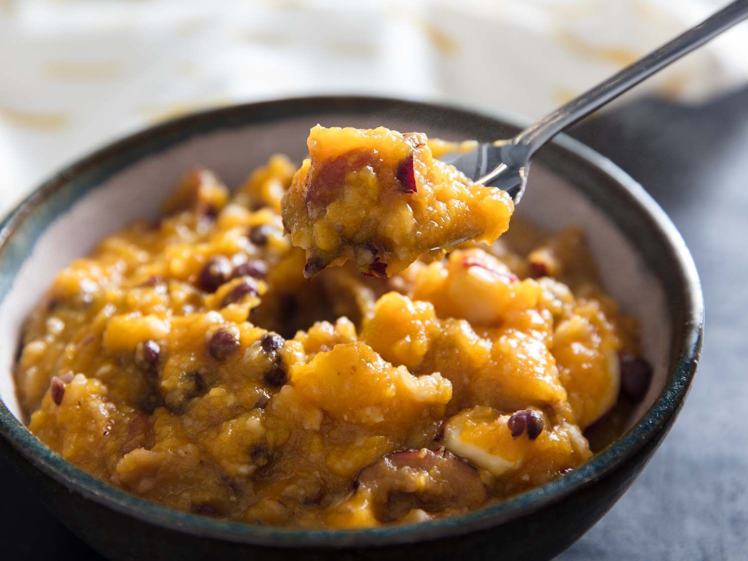 A spoonful of hobak beombeok (Korean pumpkin porridge) being lifted from a bowl