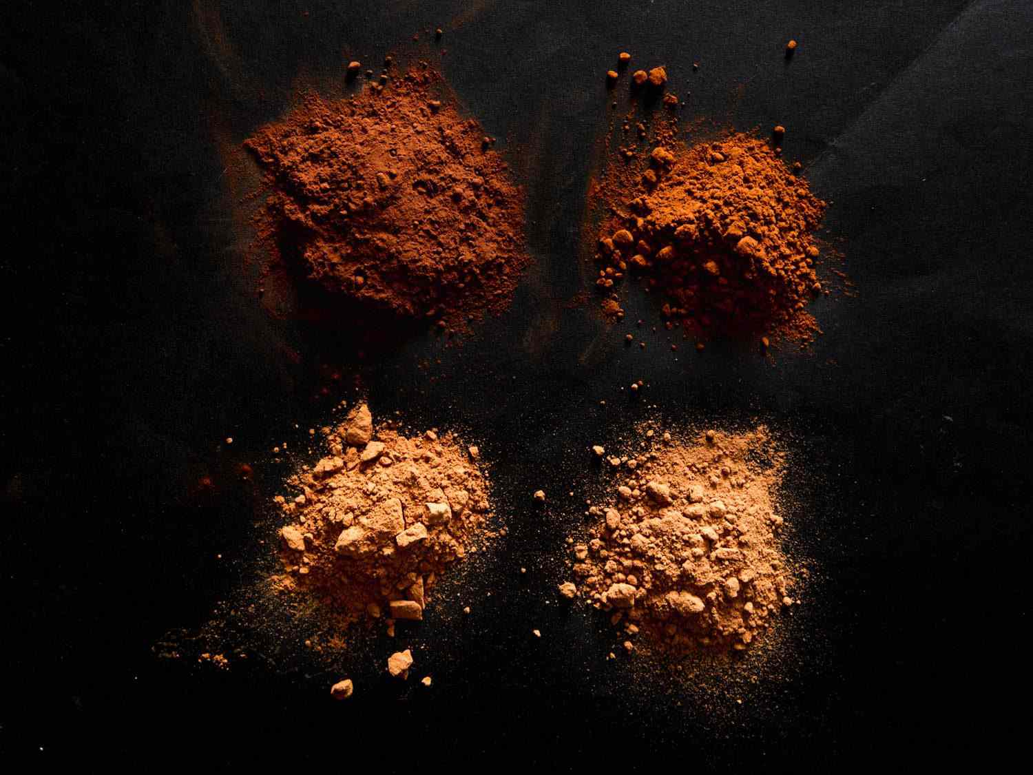 Four mounds of cocoa powder on a black surface: Clockwise from top left: Cacao Barry, Divine, Hershey's, Nestlé.