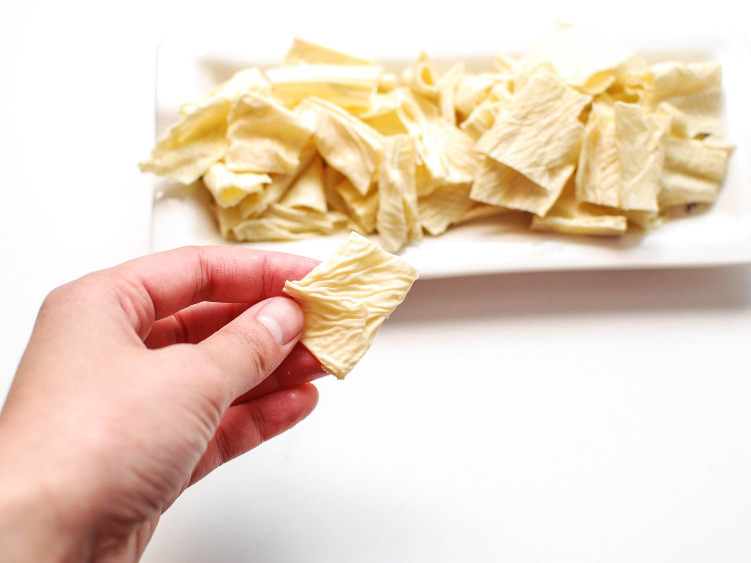 A platter of rehydrated bean curd sticks, with a hand picking up a piece.