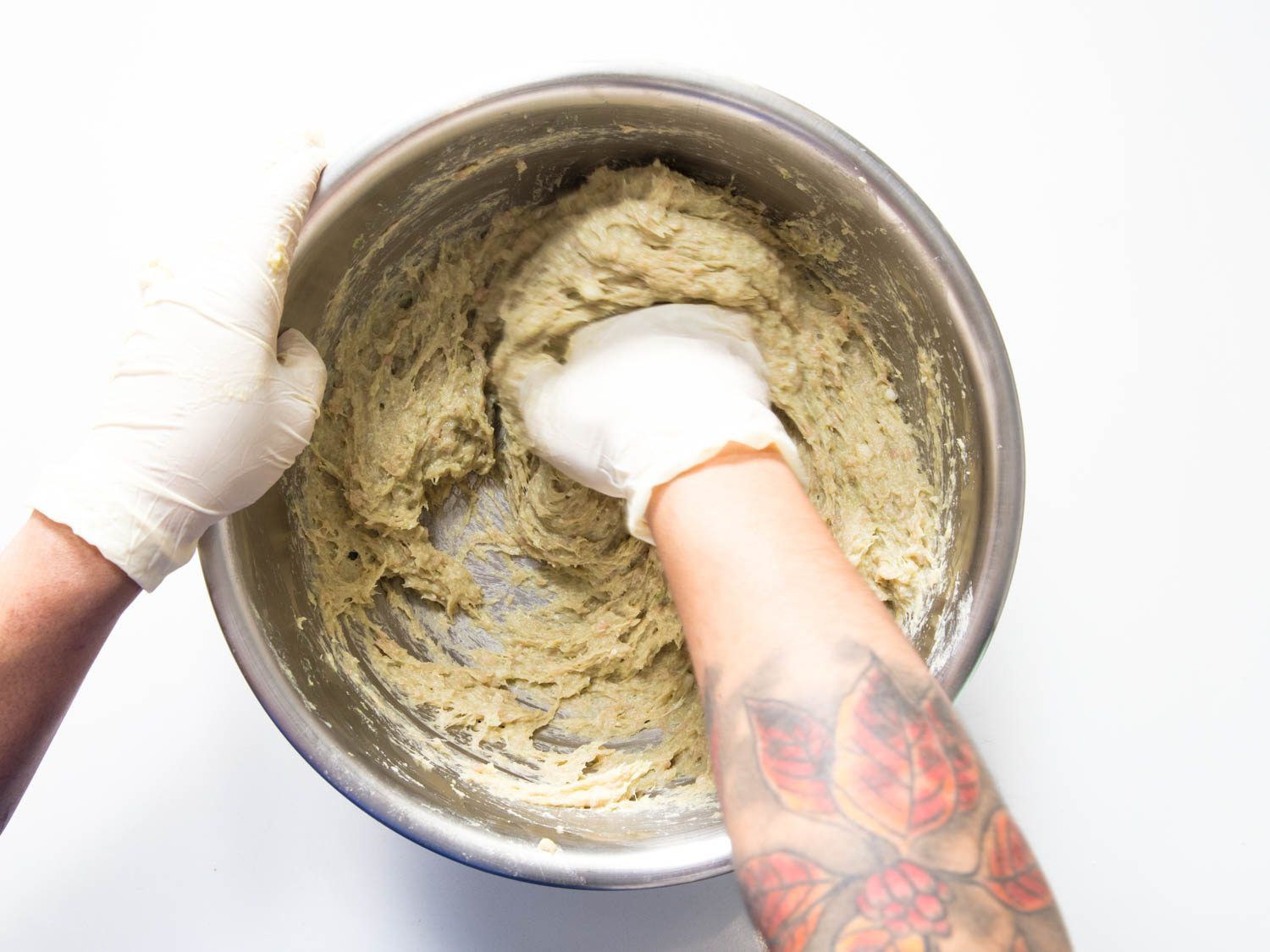 The meatball mixture is thoroughly mixed by gloved hands in a mixing bowl.