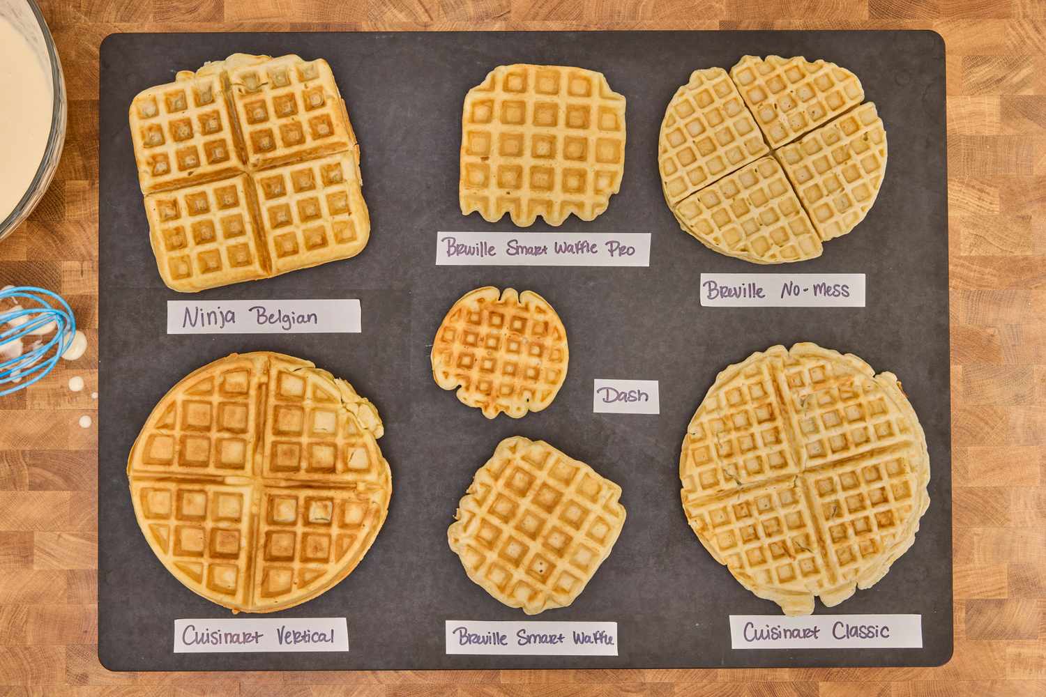 A variety of cooked waffles, labeled with tape underneath each one, sitting on a black surface