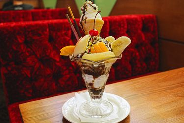 A dessert parfait served in a glass dish with fruit and toppings on a wooden table