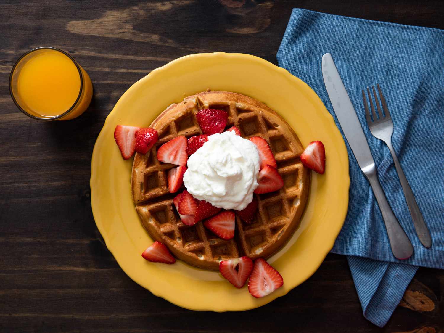 A yeasted buttermilk waffle on a plate and topped with whipped cream and strawberries.