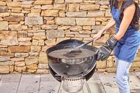 A person using a brush to clean the Weber Original Kettle Premium 22-Inch Charcoal Grill