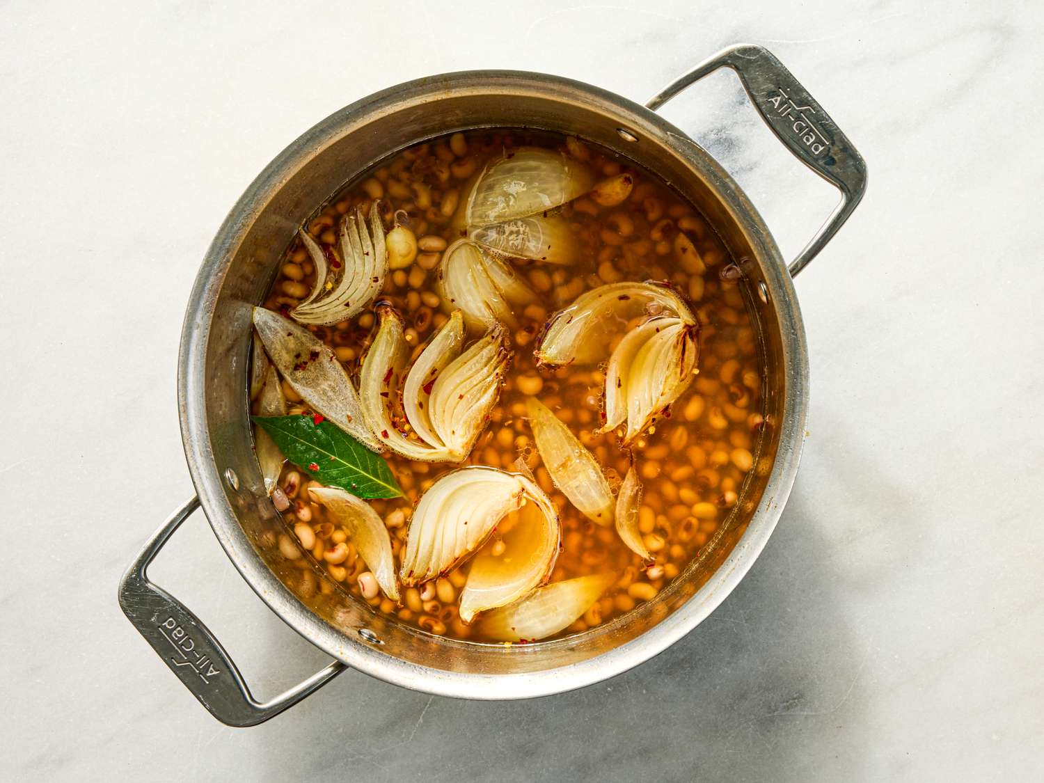 A pot containing cooking liquids onion wedges and beans