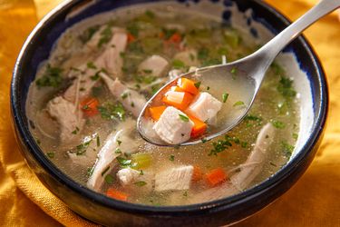 A bowl of chicken soup with a spoon holding a bite of meat and vegetables