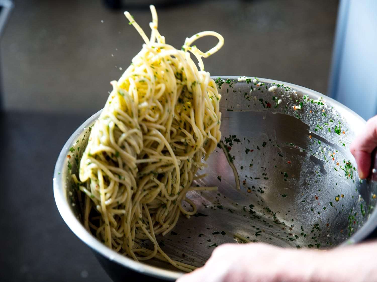 Tossing the pasta in a large bowl to emulsify the sauce and coat the spaghetti.