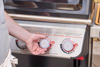 A hand turning the middle nob on the Weber Spirit EP-435 Gas Grill